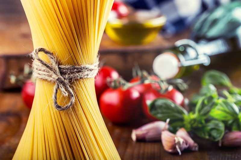 A bundle of spaghetti tied with string beside ripe tomatoes, basil, garlic and olive oil
